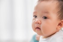 Primer plano retrato de hermosa asiático bebé mirando lejos en casa - foto de stock