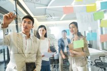 Blick durch das Glas junger asiatischer Geschäftsleute, die während eines Meetings im Büro Notizen machen — Stockfoto