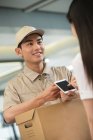 Schnappschuss eines lächelnden jungen Kuriers mit Pappschachtel, der Geschäftsfrau mit Smartphone im Büro ansieht — Stockfoto