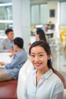 Beautiful young asian businesswoman smiling at camera while colleagues sitting behind in office — Stock Photo