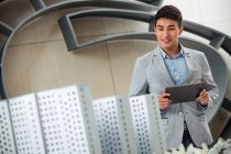 Sorridente jovem arquiteto masculino segurando tablet digital e olhando para o projeto no escritório — Fotografia de Stock