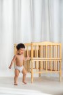 Adorable happy baby in diaper walking near crib in bedroom — Stock Photo