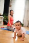 Adorable asian baby crawling on floor while mother meditating behind at home — Stock Photo