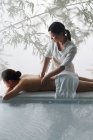 Высокий угол обзора женского массажера, делающего массаж тела молодой женщине в спа — стоковое фото