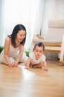 Щаслива молода азіатська мати дивиться на її прекрасну дитину, що повзає на підлозі вдома — стокове фото