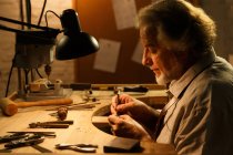 Вид сбоку сосредоточенного зрелого ювелира, работающего с инструментами в мастерской — стоковое фото