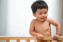 Entzückendes asiatisches Kleinkind in Windel steht im Kinderbett und schaut zu Hause weg — Stockfoto