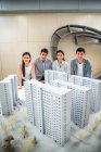 Hochwinkelaufnahme von professionellen jungen asiatischen Architekten, die in der Nähe von Gebäuden Modelle stehen und im Büro in die Kamera lächeln — Stockfoto