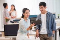 Sourire jeune asiatique homme d'affaires et femme d'affaires en utilisant la tablette numérique ensemble dans le bureau moderne — Photo de stock