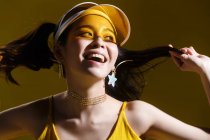 Attrayant heureux asiatique fille en chapeau transparent et en forme d'étoile boucles d'oreilles souriant et regardant loin en studio — Photo de stock