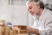 Professional focused mature architect working with blueprint and building model at workplace — Stock Photo