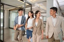 Усміхнені молоді азіатські бізнесмени і бізнесмени розмовляють і ходять разом в офісі — стокове фото