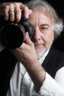 Професійний зрілий фотограф використовує фотоапарат і дивиться на камеру ізольовано на чорному — стокове фото