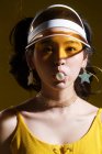 Приваблива азіатська дівчина в шапці і сережках у формі зірки, що дме бульбашкову гумку і дивиться на камеру в студії — стокове фото
