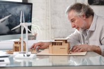 Боковой вид профессионального зрелого архитектора, работающего с моделью здания на рабочем месте — стоковое фото