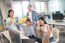 Happy young professional asian business people holding cups and working with computers in office — Stock Photo