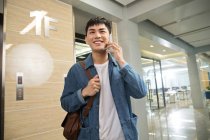 Schöner glücklicher junger asiatischer Geschäftsmann, der im Büro per Smartphone spricht — Stockfoto