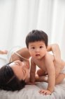 Щаслива молода азіатка лежить на ліжку і обіймає чарівну дитину — стокове фото