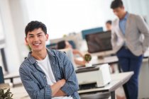 Handsome young asian businessman with crossed arms smiling at camera in modern office — Stock Photo