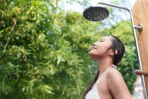 Low angle view of smiling young woman in bikini taking shower with closed eyes — Stock Photo