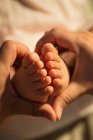Cropped shot of mother holding feet of infant baby, close-up view — Stock Photo
