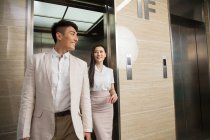 Sourire jeune asiatique homme d'affaires et femme d'affaires marche à partir de l'ascenseur ouvert — Photo de stock