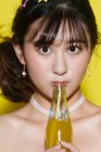 Bela jovem mulher asiática segurando garrafa de vidro com bebida amarela e olhando para a câmera no estúdio — Fotografia de Stock