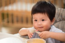 Primer plano vista de adorable asiático niño sosteniendo cuchara y comer en casa - foto de stock