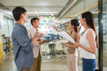Visão lateral de profissionais jovens empresários asiáticos e mulheres de negócios de pé juntos e trabalhando com papéis no escritório — Fotografia de Stock