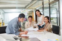 Lächelnde junge asiatische Geschäftsleute und Geschäftsfrauen, die im modernen Büro mit Papieren arbeiten — Stockfoto