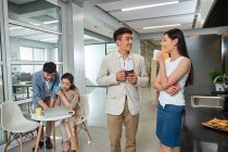 Feliz jovem asiático empresário e empresária beber café enquanto colegas usando laptop atrás no escritório — Fotografia de Stock