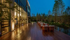 Edificio moderno con finestre e sedie illuminate sulla terrazza la sera — Foto stock