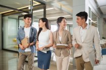 Cuatro jóvenes asiáticos empresarios caminando y hablando juntos en la oficina - foto de stock