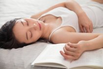 Bela jovem mulher asiática dormindo com livro na cama — Fotografia de Stock