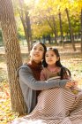 Beautiful happy asian mother and daughter sitting together and looking up in autumn park — Stock Photo