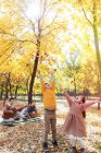 Щасливі діти грають з осіннім листям, а батьки відпочивають на картатому плед в парку — стокове фото