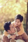 Feliz joven padre piggybacking adorable sonriente hijo en otoño parque - foto de stock