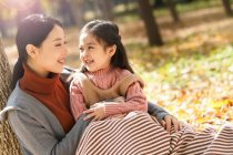Beautiful asian mother and daughter looking at each other while sitting together in autumn park — Stock Photo