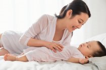 Bella sorridente giovane madre guardando bambino bambino carino che dorme sul letto — Foto stock