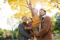 Baixo ângulo vista de feliz jovem asiático família com dois filhos olhando para cima no outono parque — Fotografia de Stock