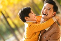 Счастливый азиатский отец и сын обнимаются в осеннем парке — стоковое фото