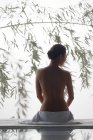 Rückansicht einer nackten jungen Frau, die auf einem Massagetisch im Spa sitzt — Stockfoto