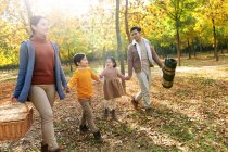 Happy family with picnic basket holding hands and walking in autumn forest — Stock Photo