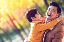 Happy asian father and son hugging in autumn park — Stock Photo
