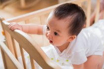 Удивленный маленький азиатский ребенок склоняется к кроватке и смотрит в сторону дома — стоковое фото