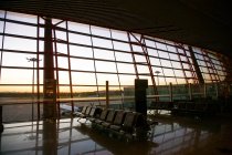 View of planes through window from empty airport lounge during sunset — Stock Photo