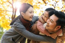 Низкий угол обзора счастливых родителей и дочки, обнимающихся в осеннем парке — стоковое фото