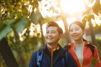 Glückliches junges asiatisches Paar mit Rucksäcken, die im Park wegschauen — Stockfoto