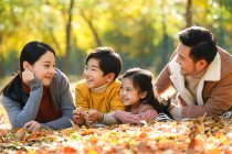 Pais jovens felizes com dois filhos deitados juntos e sorrindo uns aos outros no parque de outono — Fotografia de Stock
