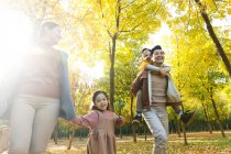Bajo ángulo vista de feliz joven asiático familia con picnic cesta caminando en otoño parque - foto de stock
